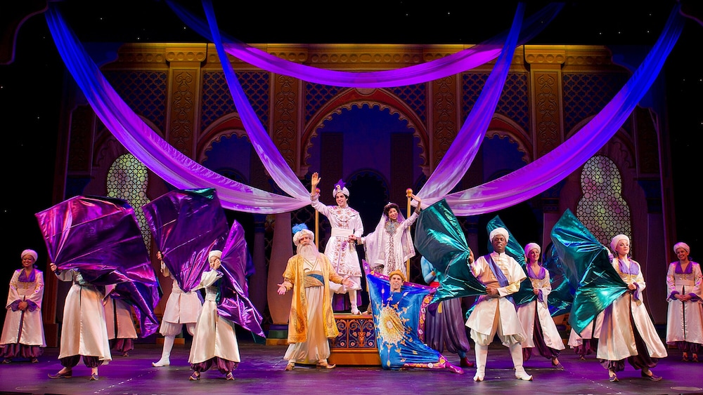 Aladdin, Princess Jasmine, the Sultan and the Magic Carpet wave on stage at Disney's Aladdin A Musical Spectacular