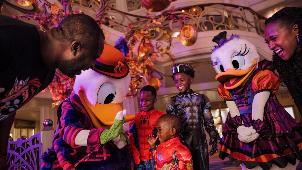 Donald Duck and Daisy Duck in Halloween costumes interacting with a family aboard a Disney cruise ship