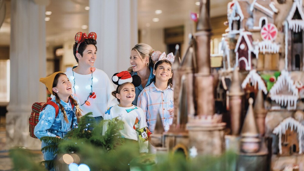Two women and 3 children smiling in wonder at an elaborate gingerbread castle display
