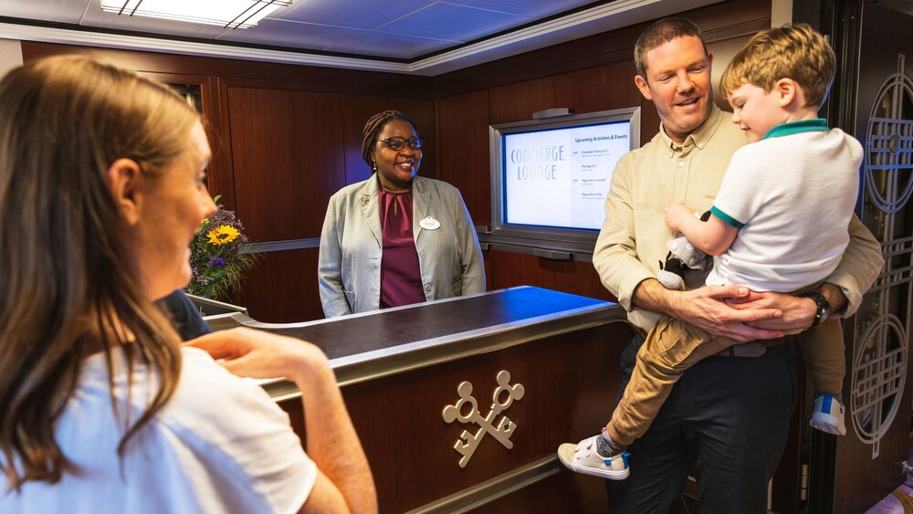 A father holding his son in his arms and a Cast Member at a Concierge desk