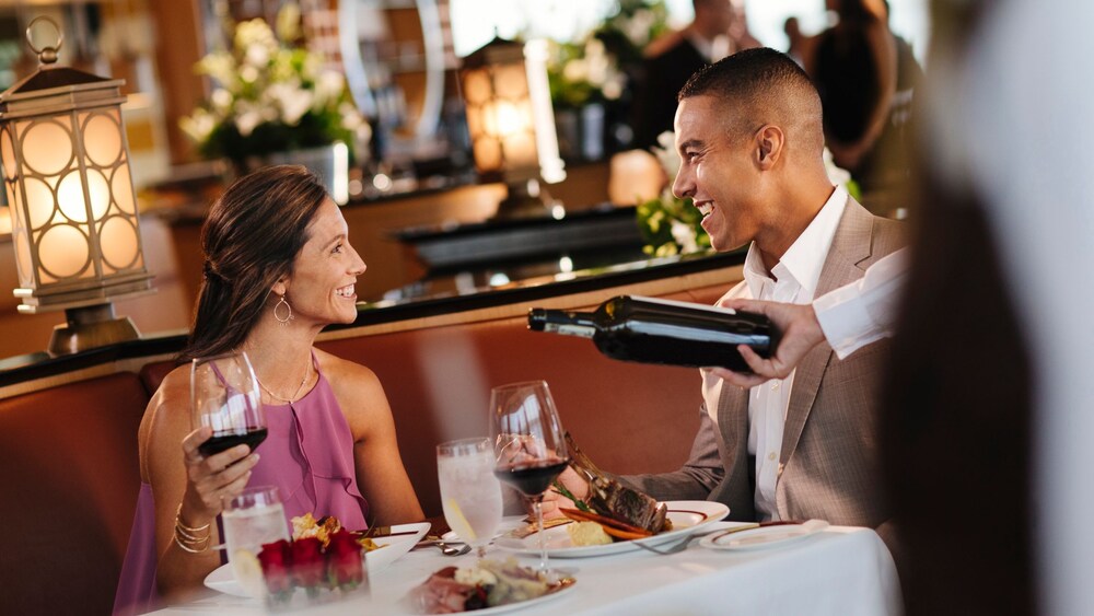 A couple eating dinner together at a dining table while a Cast Member pours a glass of wine