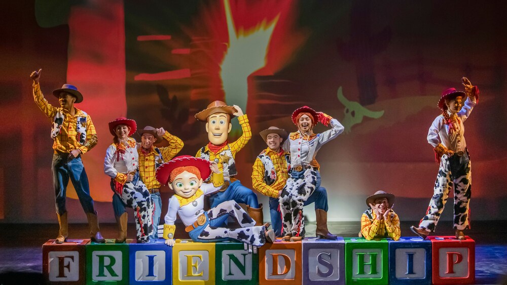 Woody, Jessie and performers dressed like them stand on top of blocks that spell out 'friendship' during Toy Story The Musical
