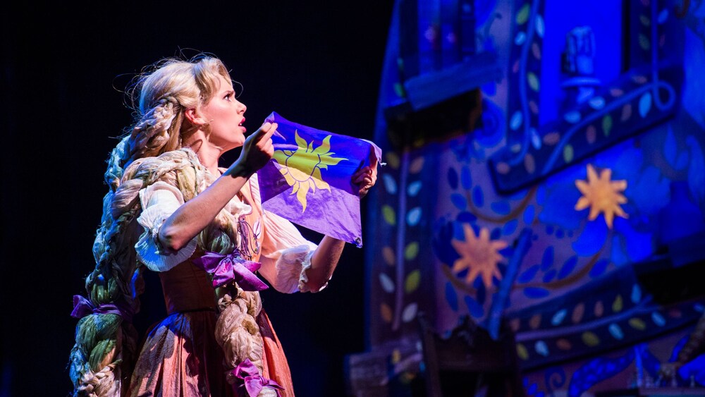 Rapunzel holding a flag with a sun icon in Tangled, The Musical 