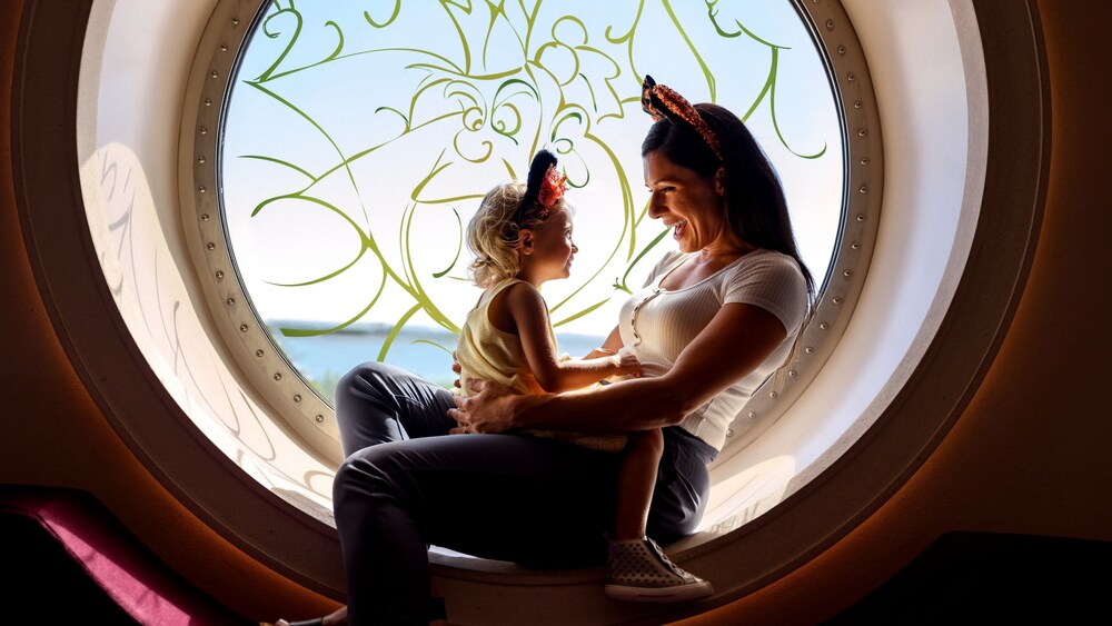 A woman holding a young girl while sitting in front of a window painted with the Queen of Hearts