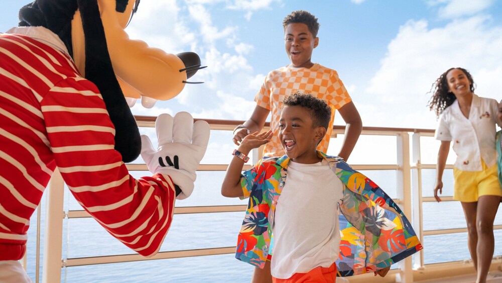 A woman and 2 boys approaching Goofy, who is giving a high five to the youngest child