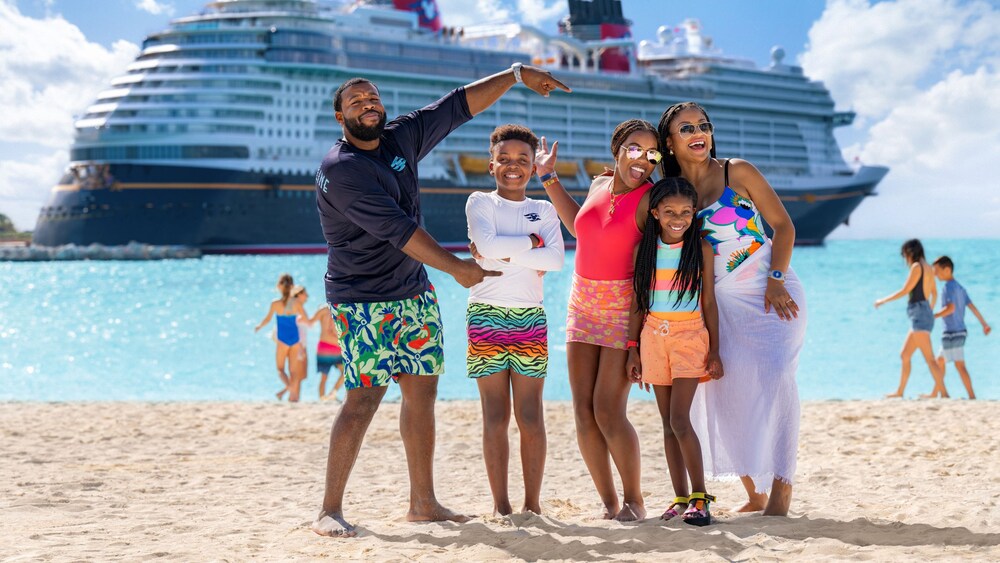 A family of 5 posing on a beach in front of a Disney Cruise Line ship