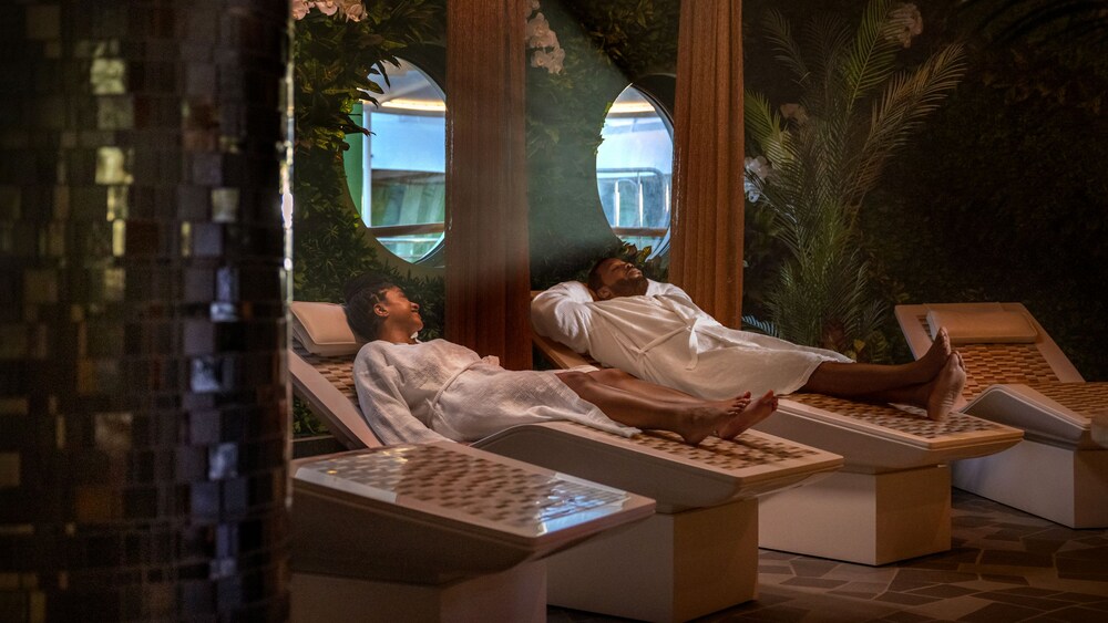 A man and a woman relaxing on reclined chairs in a spa decorated with foliage