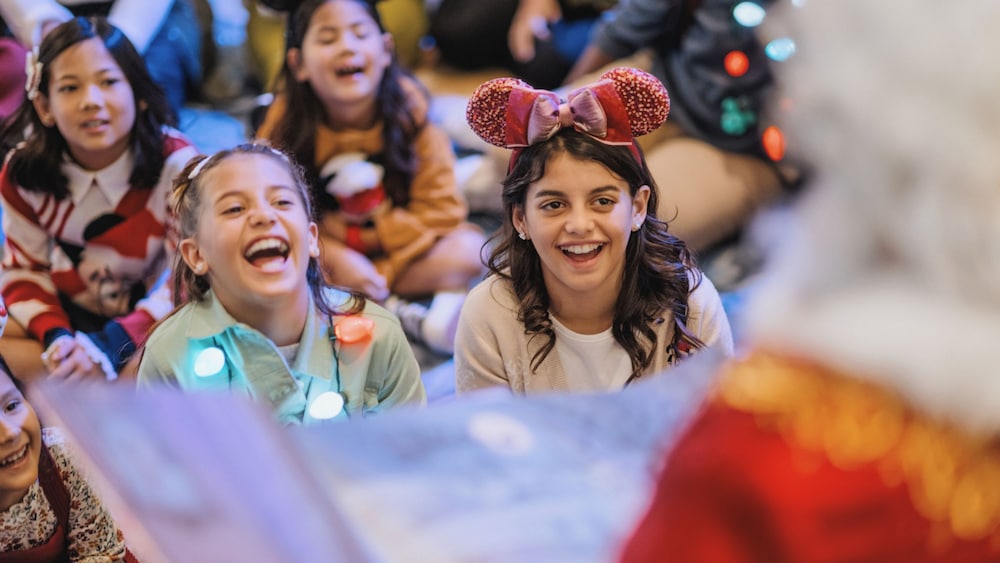 Kids laughing while wearing holiday accessories as Santa Claus reads them a story