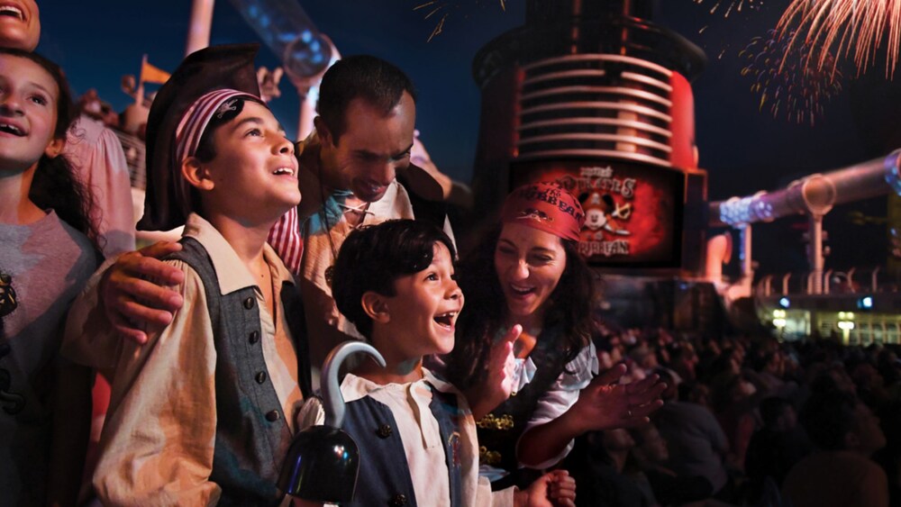 A family dressed for Pirate Night watching fireworks burst above the ship