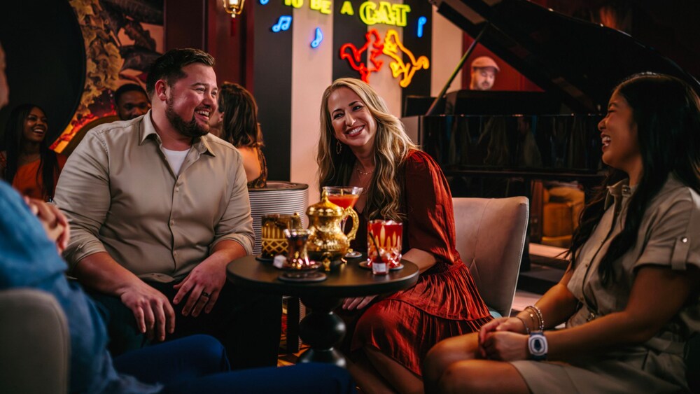 Guests smiling and enjoying beverages as a pianist plays onstage at Scat Cat Lounge
