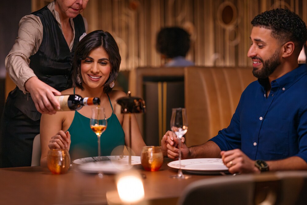 Cast Member pouring wine for a couple sitting at a table at Palo Steakhouse