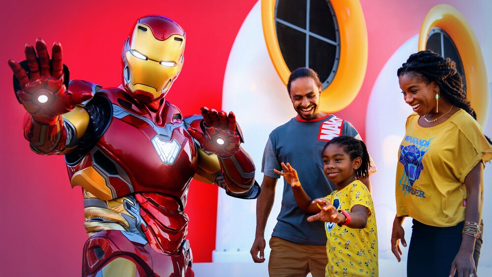 Deux clients et leur enfant posant avec Iron Man à côté de la cheminée d’un bateau de croisière Disney
