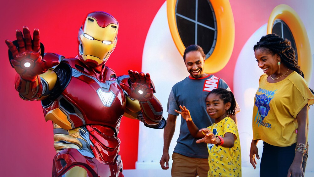 Twee gasten en hun kind poseren met Iron Man naast een schoorsteen van een schip van Disney Cruise Line