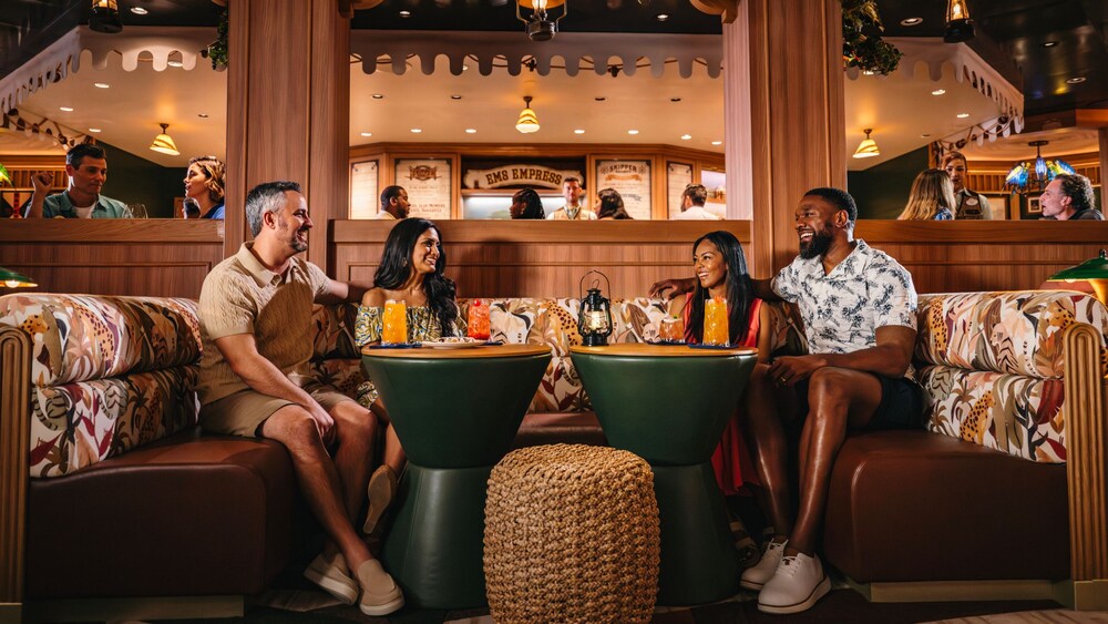 Huéspedes sonriendo mientras están sentados en las mesas con bebidas en Skipper Society, un salón en el Disney Treasure
