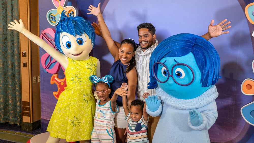 A young family of 4 posing with Joy and Sadness from Inside Out