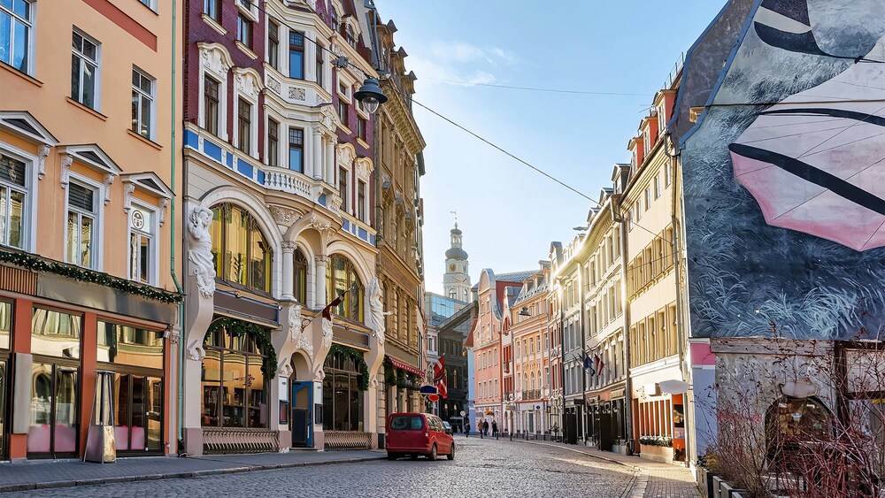 Ornate art nouveau buildings with statues lining a narrow cobblestone street with a distant tower