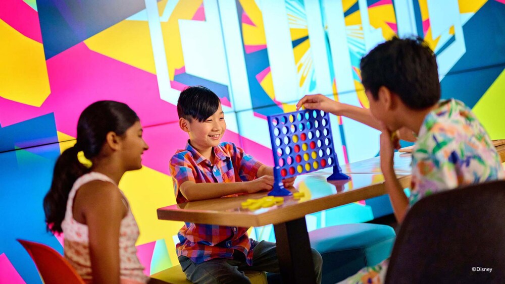 Three children playing Connect 4 inside Edge, a tween club on board the Disney Adventure