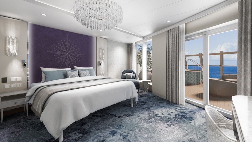 A Concierge Royal Suite with a king size bed, a chandelier and glass doors that open to an oceanview verandah