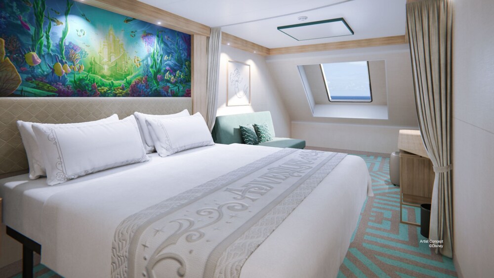 A Deluxe Oceanview Stateroom with a bed, a sofa, privacy curtains, Disney artwork on the walls and a window