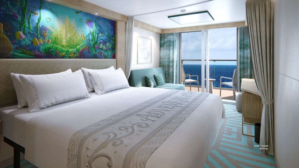 A Deluxe Oceanview Stateroom with a bed, a sofa, Disney artwork on the walls and glass doors that open to a verandah