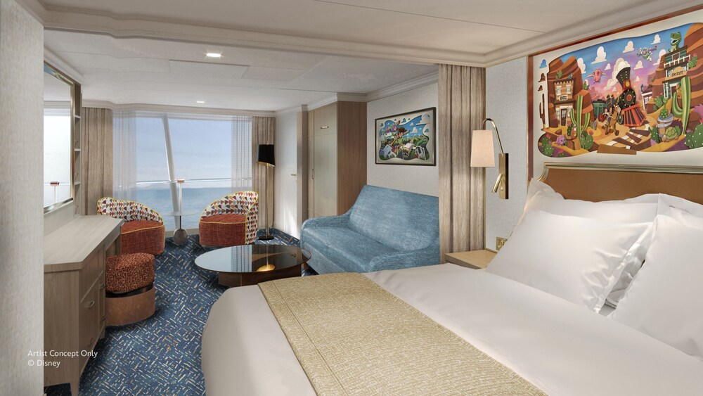 A Concierge oceanview stateroom on the Disney Believe cruise ship, featuring a bed and sofa with chairs overlooking a large window