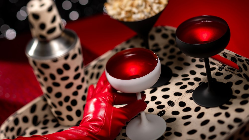 A gloved hand picking up a beverage from a dalmatian spotted tray with a cocktail shaker and a popcorn filled martini glass at De Vil’s lounge