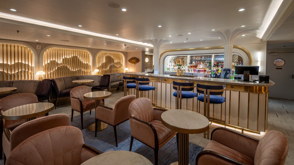 A bar with stools, chairs and tables in the Disney Dream Concierge Lounge