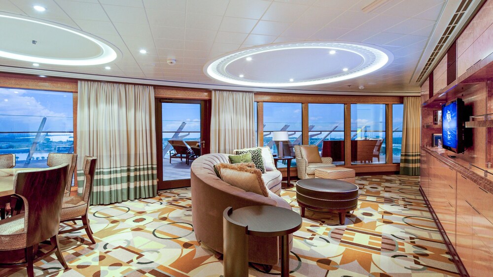 A section in a Disney Dream Concierge Royal Suite with Verandah including a dining table, a sofa, chairs, a TV and a verandah with ocean views