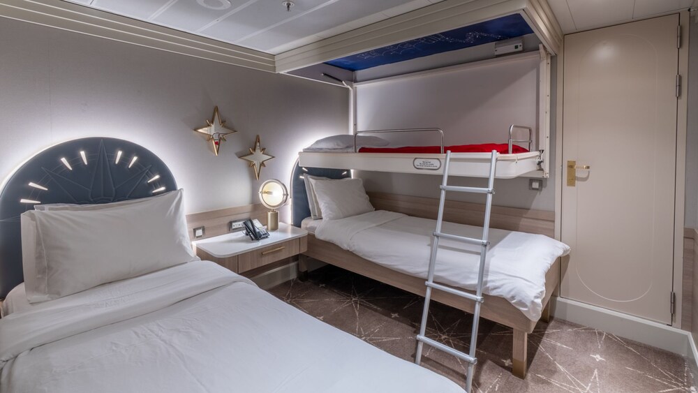 A bedroom with 2 beds, a bunk bed and a nightstand in a Disney Magic Concierge 2 Bedroom Suite with Verandah
