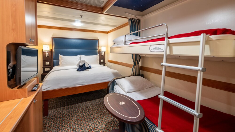 A Disney Magic Standard Inside Stateroom with a desk, table, bed, 2 bunk beds and 2 nightstands