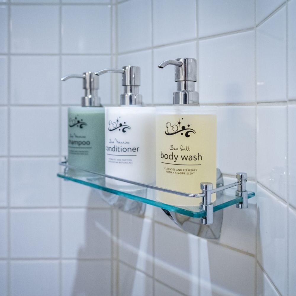 A bathroom with a shower shelf containing shampoo, conditioner and body wash in a Disney Magic Deluxe Oceanview with Verandah Stateroom