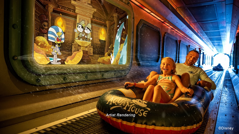 A boy and a girl laughing while riding in an inflatable raft through a tunnel with Mickey Mouse cartoons displayed on the walls