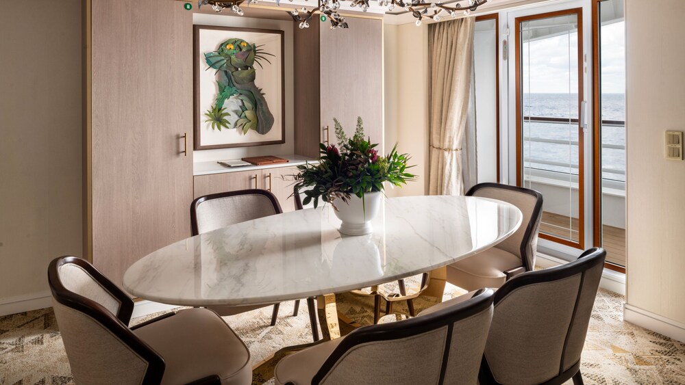 An artist rendering of a Disney Treasure 1 Story Royal Suite with Verandah Stateroom living room with a dining table and a verandah with an ocean view