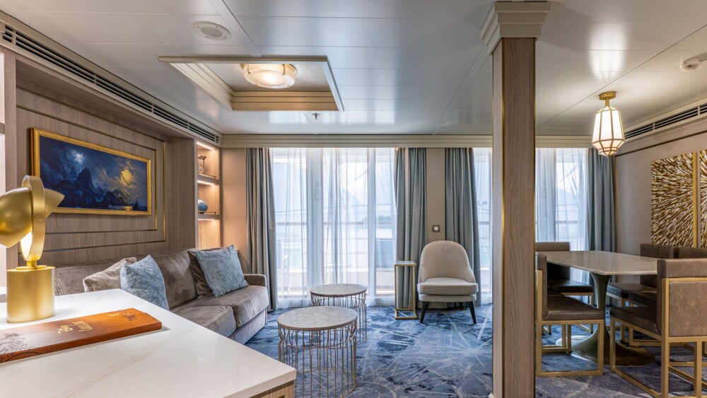 A living area with a sofa, credenza, chair, verandah, 2 coffee tables and a dining table with chairs in a Disney Wonder Concierge 2 Bedroom Suite with Verandah