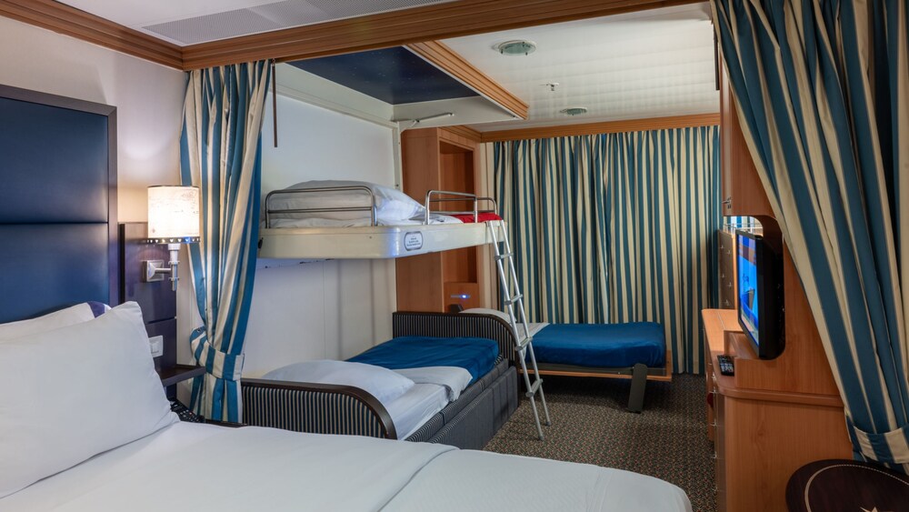 A Disney Wonder Deluxe Family Oceanview with Verandah Stateroom with a bed, table, nightstand, desk, TV, 2 bunk beds and a wall bed