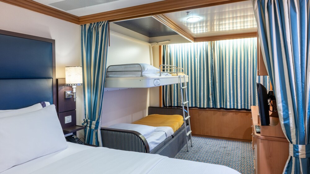 A Disney Wonder Deluxe Oceanview Stateroom with a bed, nightstand, desk, TV and 2 bunk beds