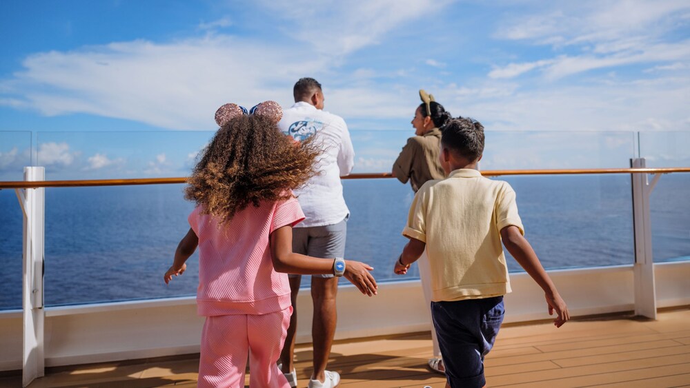 2 kids joining their parents at a Disney Cruise Line ship’s railing overlooking the sea