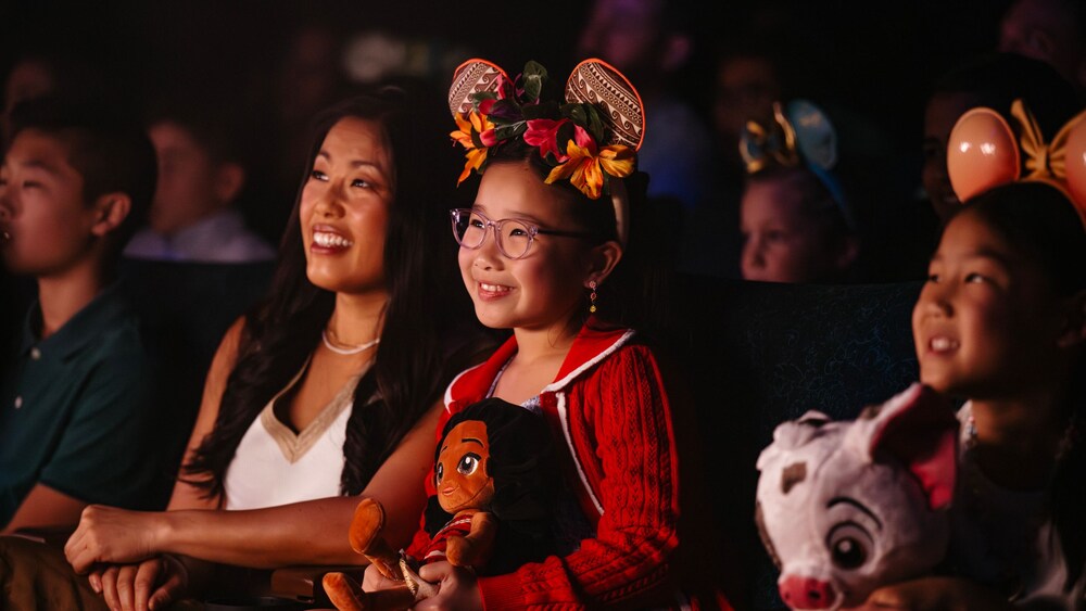 2 girls in Mickey ear headbands, watching a show in a theater with their mother