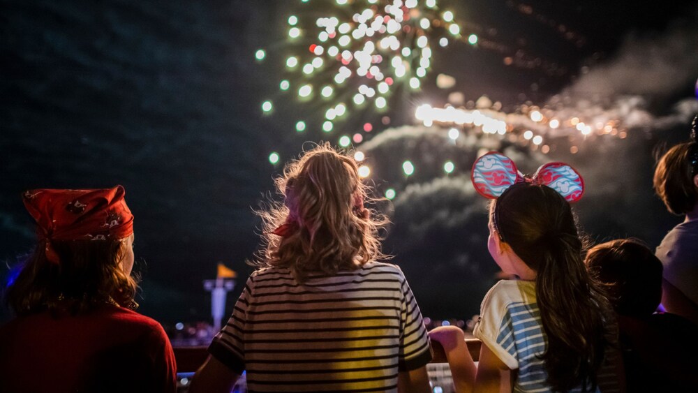 3 kids watching fireworks from a Disney Cruise Line ship’s railing at night