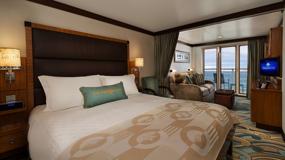 A Disney Fantasy Verandah Stateroom with a bed, chair, table, sofa, desk, TV, 2 nightstands and a verandah facing the ocean