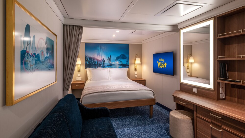 A Disney Wish Inside Stateroom with a bed, sofa, desk, mirror, TV, 2 nightstands and artwork inspired by Cinderella
