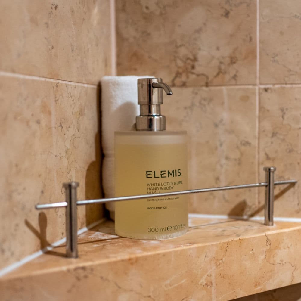 Elemis hand and body wash on a shelf in a marble shower