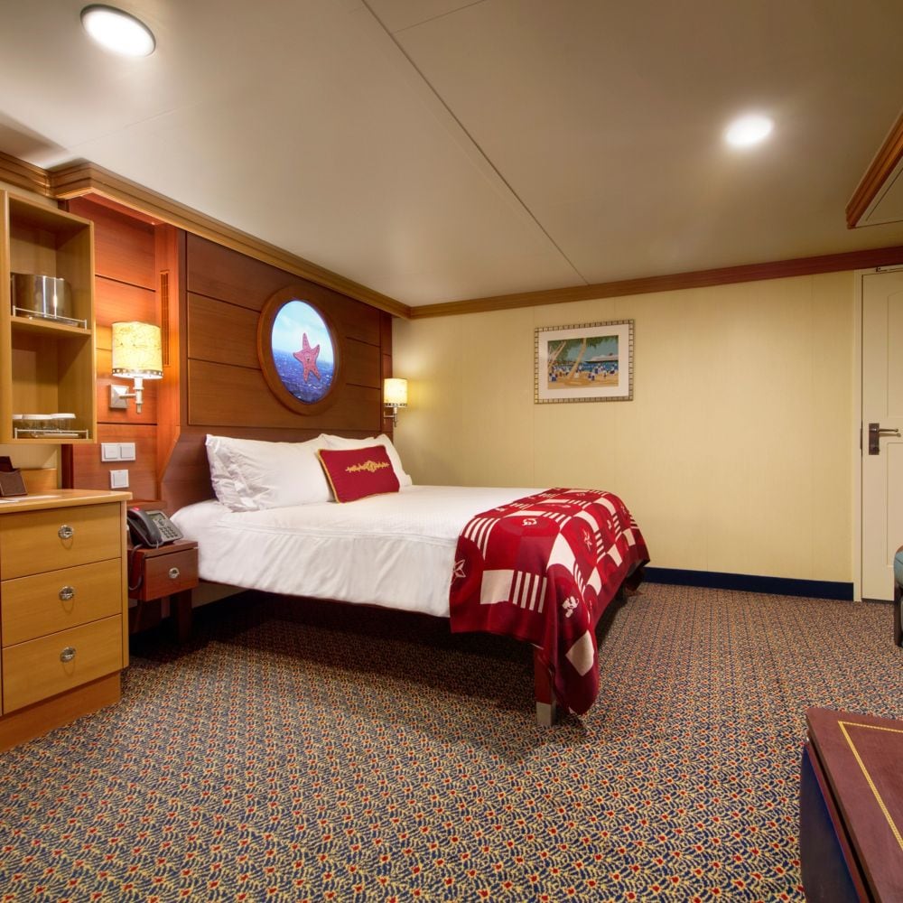 A Disney Cruise Line stateroom with a desk, storage shelves, a nightstand, a bed and a virtual porthole