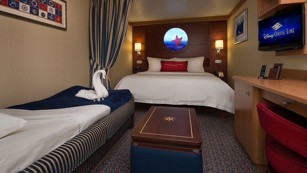 A Disney Cruise Line Deluxe Inside Stateroom with a low table, a sleeper sofa, a bed, a virtual porthole, storage shelves, a TV, a mirror and a desk