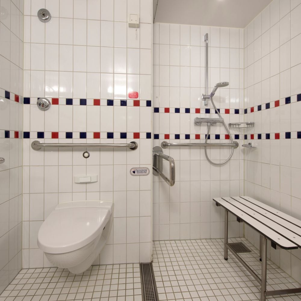 An accessible bathroom in a Disney Cruise Line Stateroom with a toilet, a walk in shower and a bench