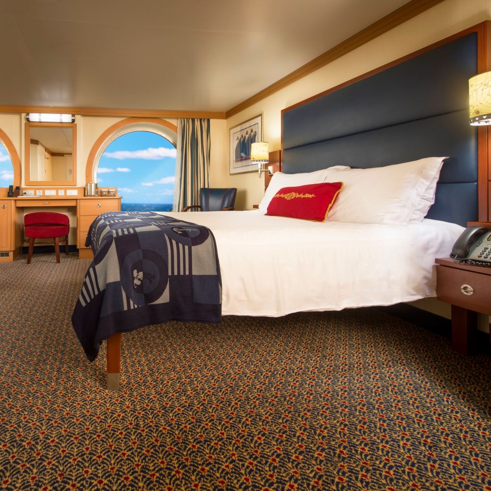 A Disney Cruise Line stateroom with a desk, a mirror, a porthole with an ocean view, a chair and a bed
