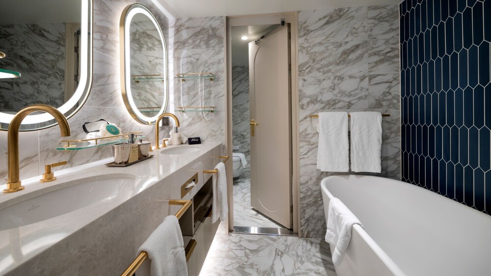 A Disney Cruise Line Concierge 2 Bedroom Suite with Verandah bathroom with a bathtub, towels, 2 sinks, 2 mirrors and marble accents