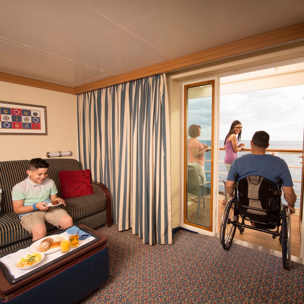 A family in a stateroom with one family member rolling their wheelchair onto a verandah 
