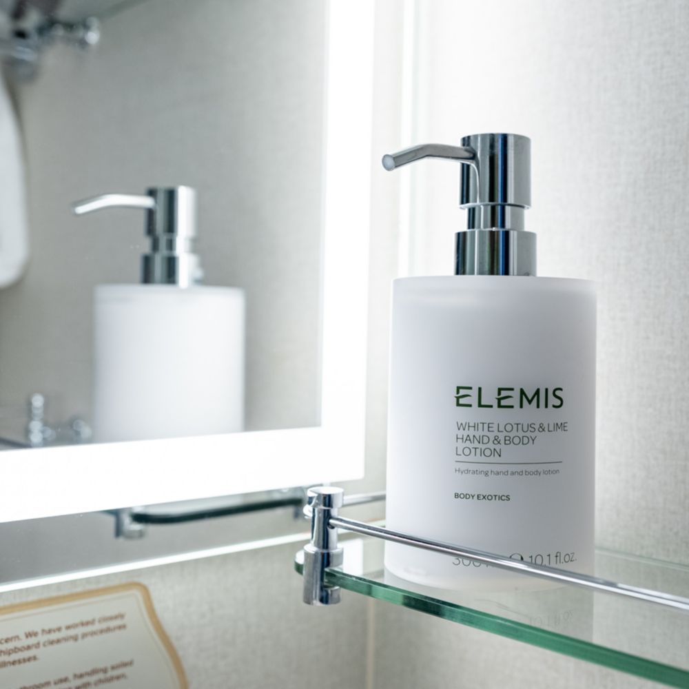 A glass shelf in a bathroom containing Elemis hand and body lotion in a Disney Cruise Line Stateroom