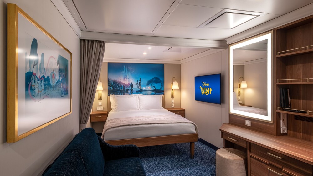 A Disney Wish Inside Stateroom with a bed, sofa, desk, mirror, TV, 2 nightstands and artwork inspired by Cinderella